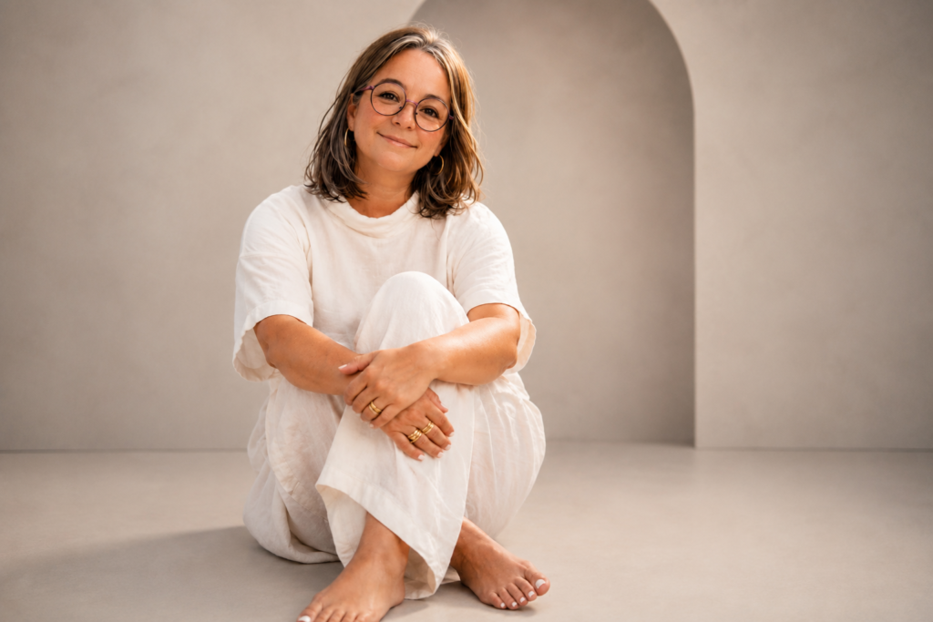 Portrait de Marie-Fred, créatrice de chemin, assise avec un sourire chaleureux dans un décor épuré, symbole d'écoute, de réflexion et d'accompagnement.